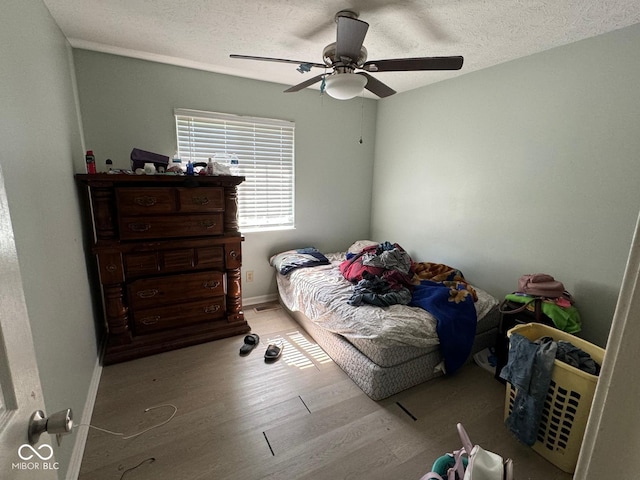 bedroom with ceiling fan, light hardwood / wood-style floors, and a textured ceiling