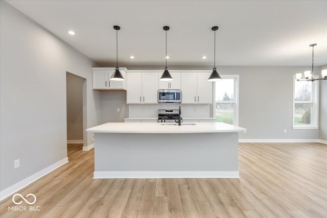 kitchen with appliances with stainless steel finishes, light wood-type flooring, a kitchen island with sink, and sink