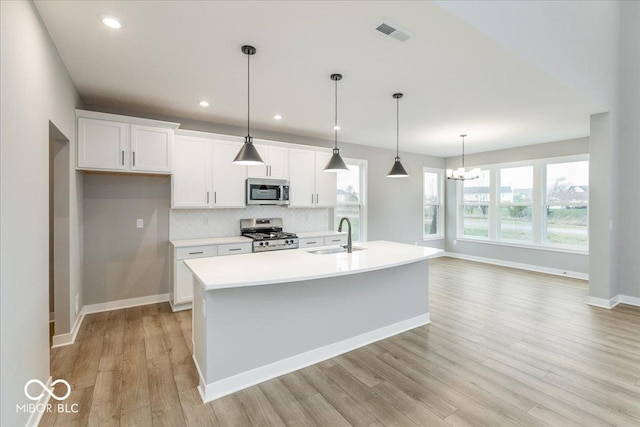 kitchen with an island with sink, stainless steel appliances, decorative light fixtures, and light wood-type flooring