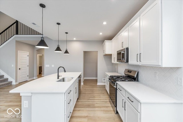 kitchen featuring a kitchen island with sink, sink, light wood-type flooring, appliances with stainless steel finishes, and decorative light fixtures