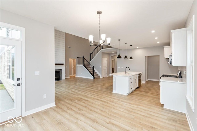 kitchen featuring a fireplace, a center island with sink, white cabinets, light hardwood / wood-style floors, and hanging light fixtures