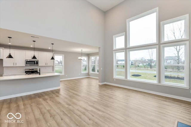 unfurnished living room featuring an inviting chandelier, a high ceiling, and light wood-type flooring