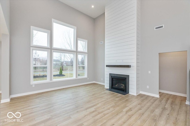 unfurnished living room featuring light wood-type flooring, a towering ceiling, and a healthy amount of sunlight