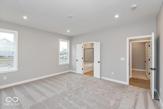 unfurnished bedroom with ensuite bathroom and light colored carpet