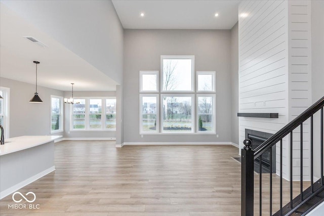 unfurnished living room with a towering ceiling, a chandelier, and light wood-type flooring