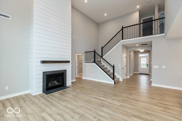 unfurnished living room with a fireplace, a high ceiling, and light hardwood / wood-style floors