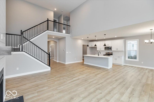 unfurnished living room featuring sink, light hardwood / wood-style flooring, a towering ceiling, and a notable chandelier