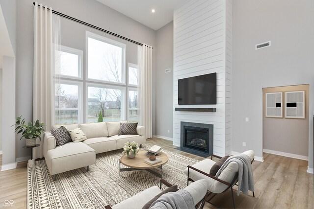 living room with a fireplace, a towering ceiling, and light hardwood / wood-style floors