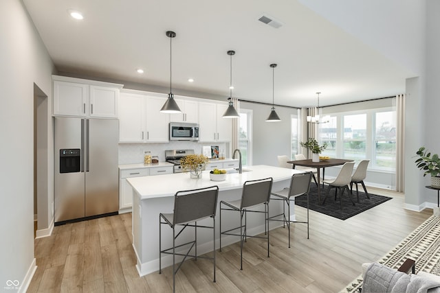 kitchen featuring stainless steel appliances, white cabinetry, a center island with sink, and light hardwood / wood-style floors