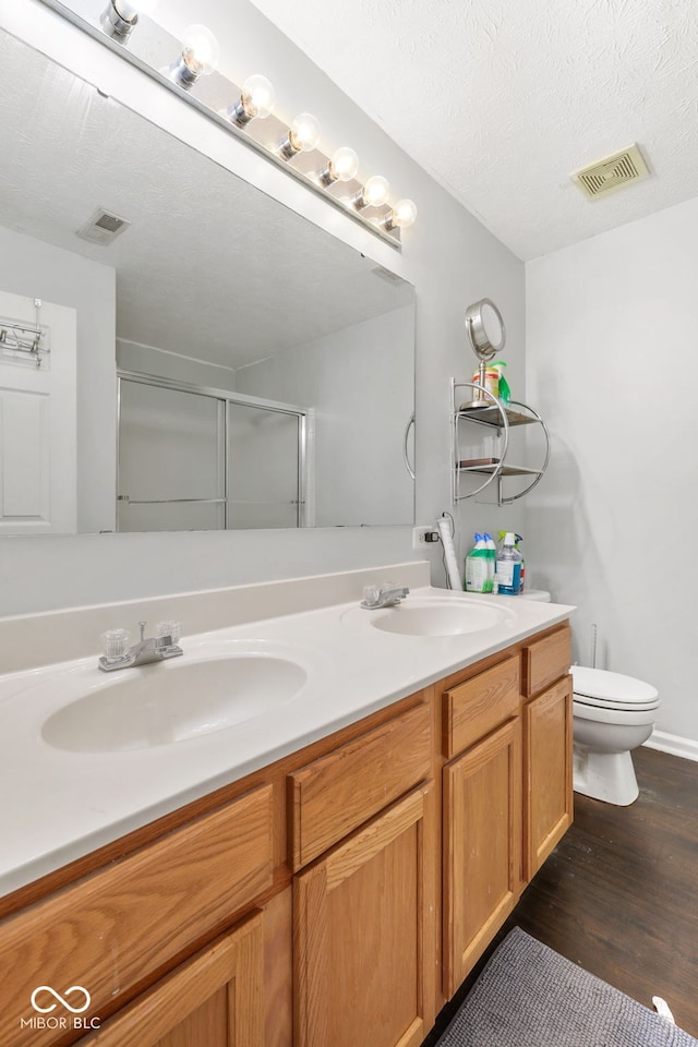 bathroom featuring a textured ceiling, toilet, double vanity, and wood-type flooring