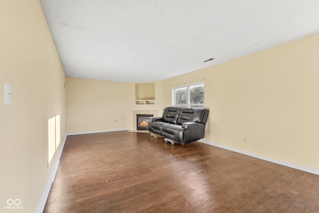 living area featuring baseboards, visible vents, dark wood finished floors, and a tile fireplace