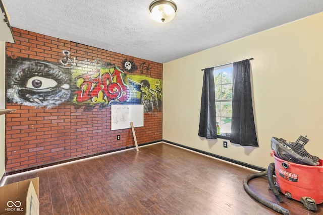 unfurnished room with a textured ceiling, brick wall, and wood finished floors