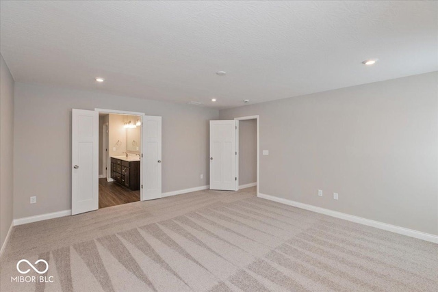 unfurnished bedroom with connected bathroom, light colored carpet, and a textured ceiling