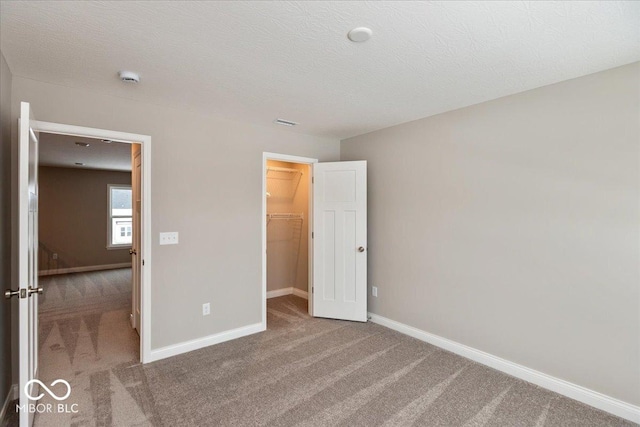 unfurnished bedroom featuring a spacious closet, carpet floors, a closet, and a textured ceiling