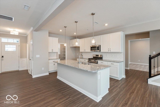 kitchen with an island with sink, white cabinetry, sink, stainless steel appliances, and light stone countertops