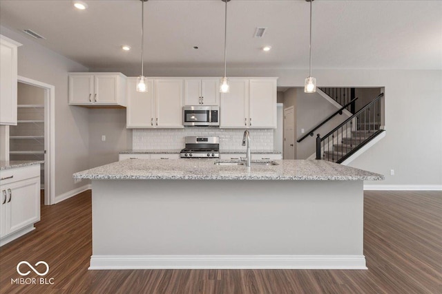 kitchen featuring sink, white cabinetry, decorative light fixtures, stainless steel appliances, and a kitchen island with sink