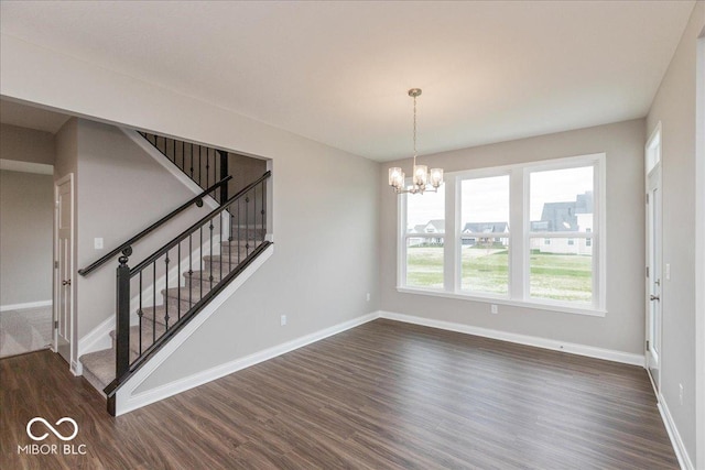 unfurnished dining area featuring baseboards, an inviting chandelier, and dark wood finished floors