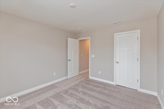 unfurnished bedroom featuring light carpet, a textured ceiling, visible vents, and baseboards
