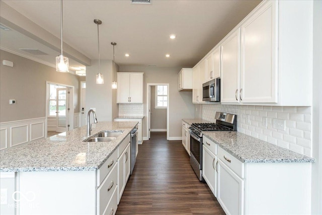 kitchen with white cabinets, stainless steel appliances, a sink, decorative backsplash, and an island with sink