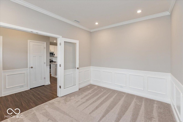 carpeted spare room featuring crown molding, wainscoting, visible vents, recessed lighting, and a decorative wall