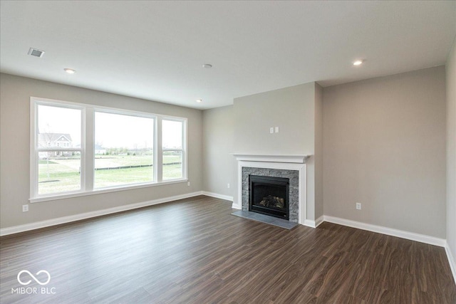 unfurnished living room featuring baseboards, a stone fireplace, dark wood-style floors, and recessed lighting