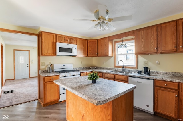 kitchen featuring a center island, brown cabinets, light countertops, a sink, and white appliances