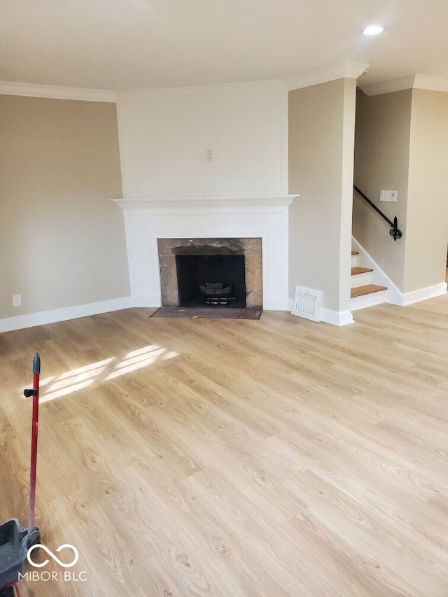 unfurnished living room featuring stairway, a fireplace with flush hearth, wood finished floors, visible vents, and ornamental molding