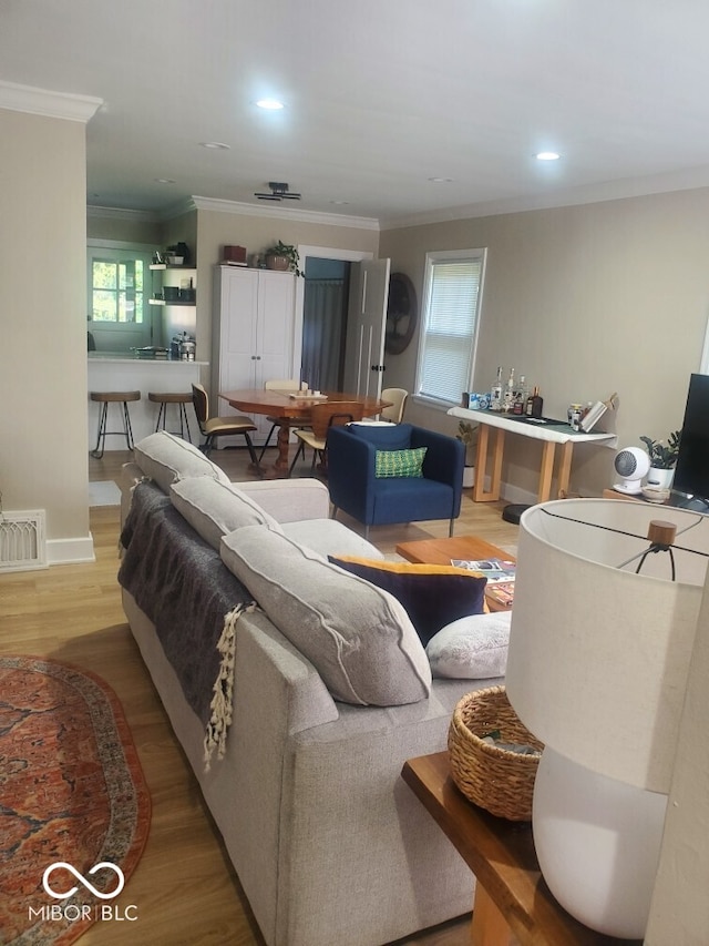 living room with ornamental molding, visible vents, plenty of natural light, and light wood finished floors