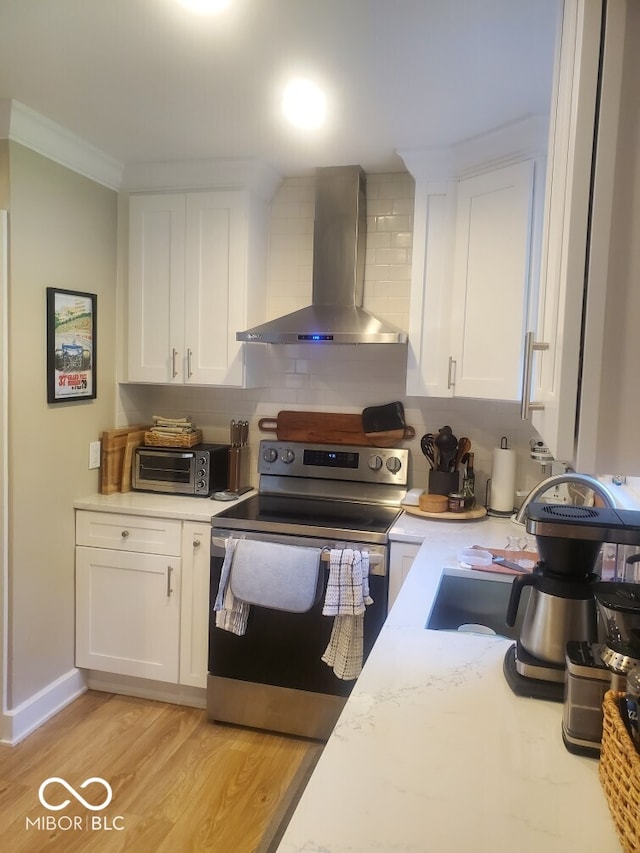 kitchen featuring light wood-type flooring, electric stove, backsplash, white cabinets, and wall chimney range hood