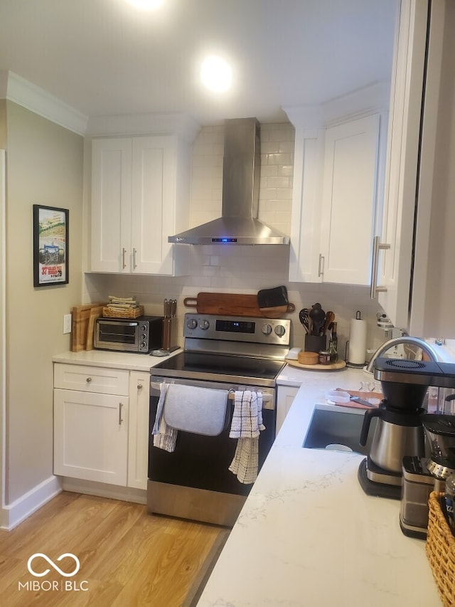 kitchen with white cabinets, light wood-style flooring, a toaster, wall chimney exhaust hood, and stainless steel electric stove