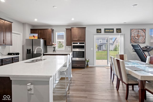 kitchen with light hardwood / wood-style floors, light stone countertops, appliances with stainless steel finishes, sink, and a center island with sink