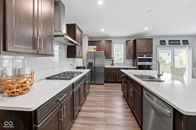 kitchen with stainless steel appliances, decorative backsplash, wall chimney exhaust hood, sink, and light wood-type flooring