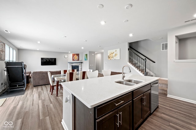 kitchen with sink, a fireplace, wood-type flooring, a kitchen island with sink, and dishwasher