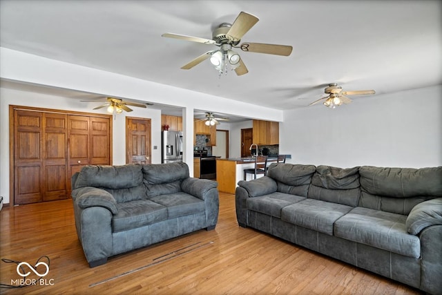 living room with ceiling fan, sink, and light hardwood / wood-style floors