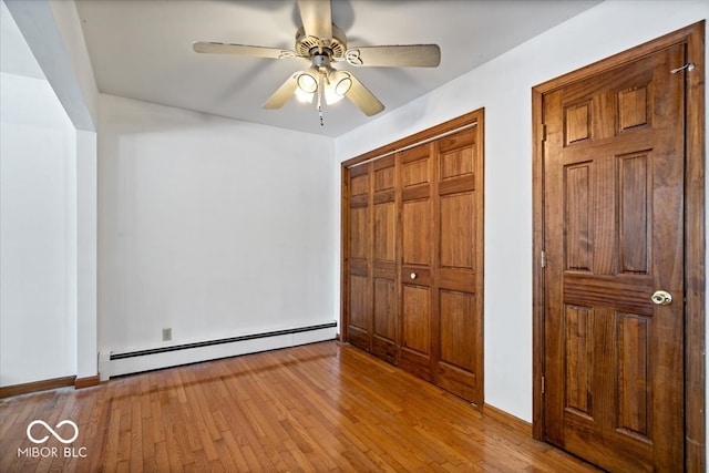 unfurnished bedroom featuring light wood-type flooring, ceiling fan, a closet, and a baseboard heating unit