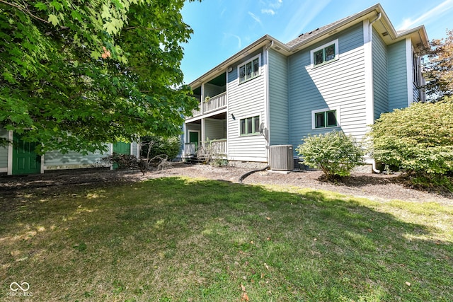 rear view of property featuring central air condition unit, a lawn, and a balcony