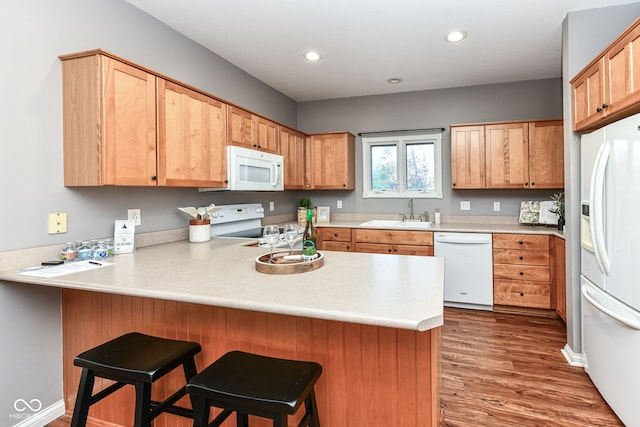 kitchen with white appliances, sink, kitchen peninsula, a kitchen breakfast bar, and dark hardwood / wood-style floors