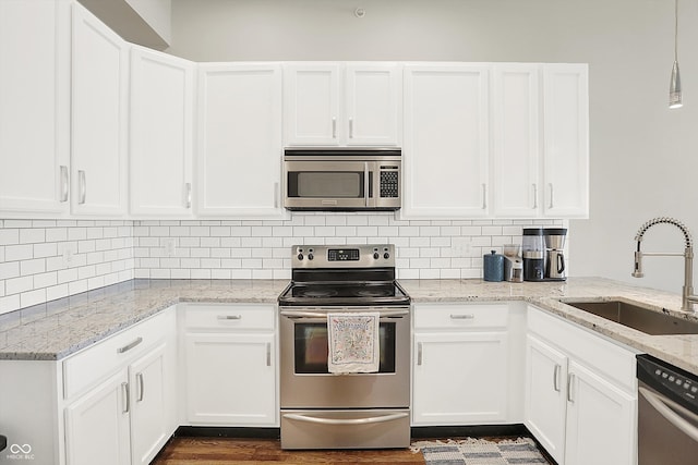 kitchen featuring hardwood / wood-style floors, white cabinetry, appliances with stainless steel finishes, hanging light fixtures, and sink