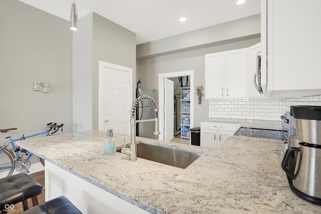 kitchen with tasteful backsplash, white cabinetry, light stone countertops, hardwood / wood-style flooring, and sink