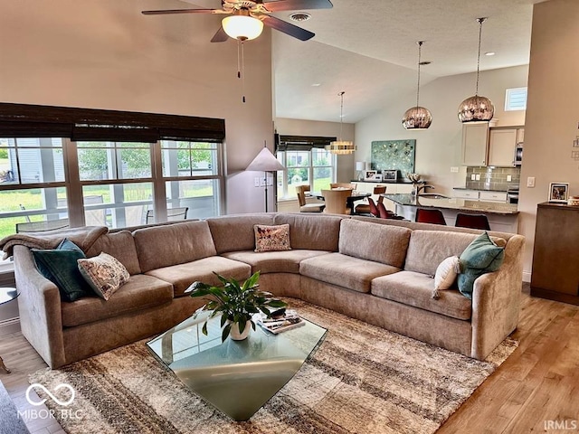 living room featuring light wood-type flooring, high vaulted ceiling, ceiling fan with notable chandelier, and sink