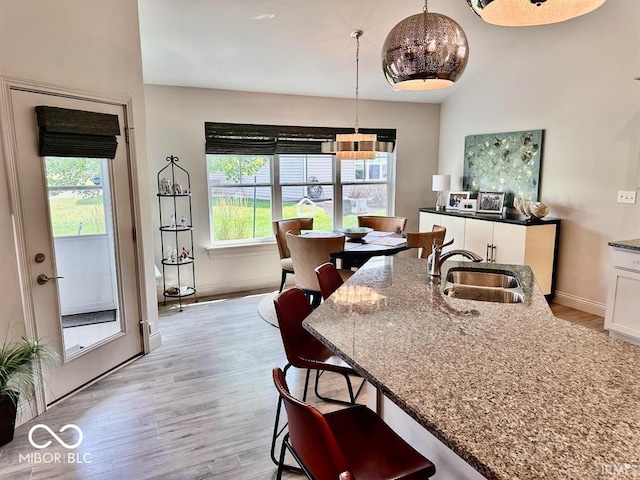 interior space with light wood-type flooring, stone countertops, a kitchen bar, sink, and decorative light fixtures