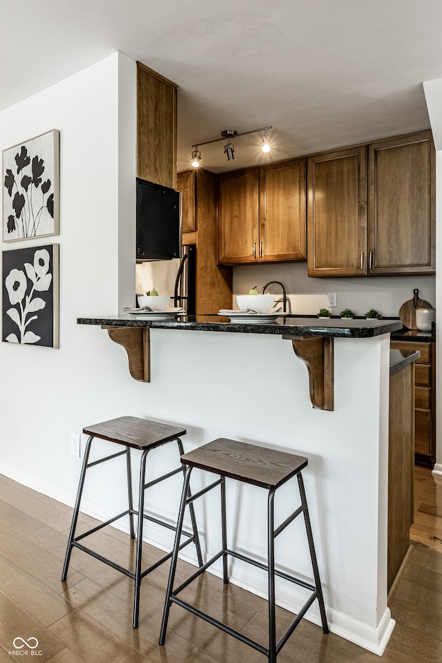 kitchen with kitchen peninsula, light hardwood / wood-style flooring, dark stone countertops, and a kitchen bar