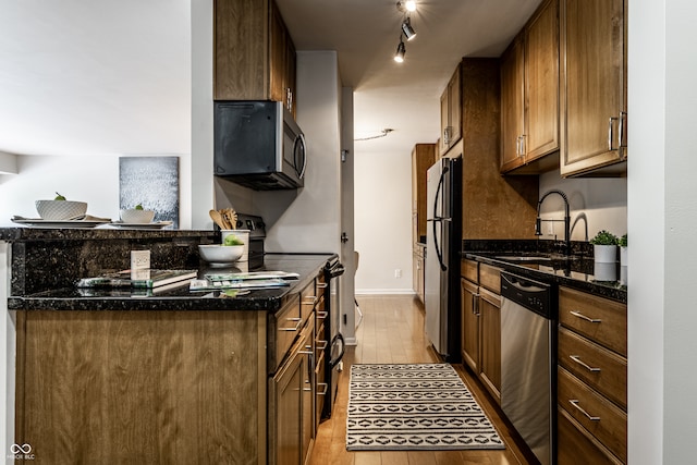 kitchen with light hardwood / wood-style flooring, track lighting, sink, dark stone countertops, and stainless steel appliances