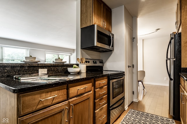 kitchen with appliances with stainless steel finishes, dark stone countertops, and light hardwood / wood-style flooring