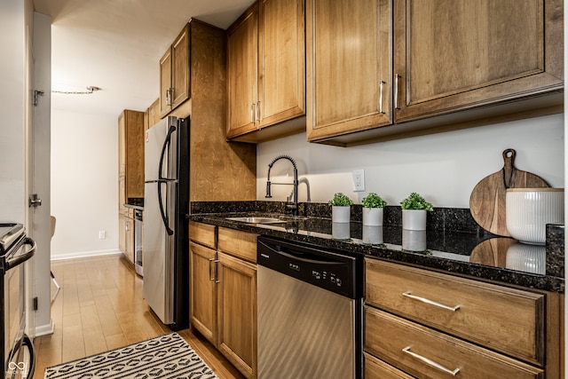 kitchen featuring light hardwood / wood-style floors, appliances with stainless steel finishes, sink, and dark stone countertops