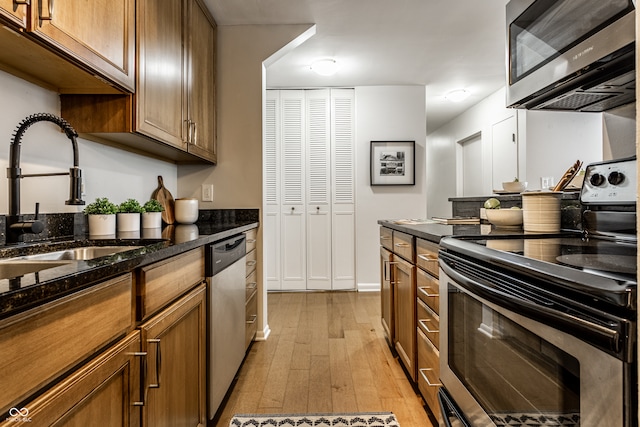 kitchen featuring sink, stainless steel appliances, light hardwood / wood-style floors, and dark stone countertops