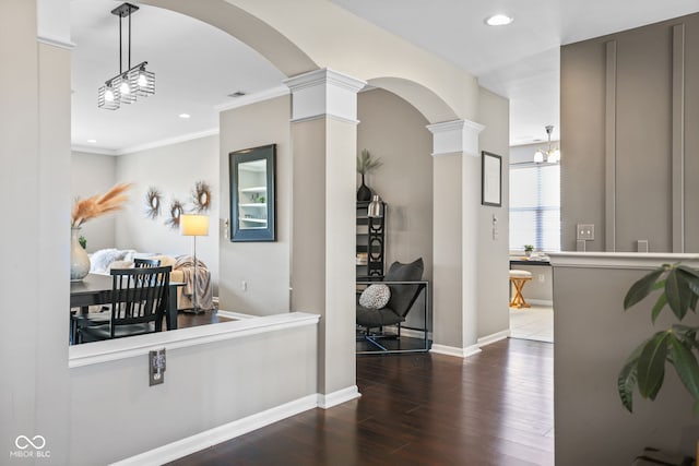 hallway featuring crown molding, dark hardwood / wood-style floors, a chandelier, and ornate columns