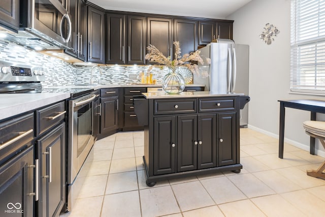 kitchen with stainless steel appliances, a center island, light tile patterned flooring, dark brown cabinetry, and tasteful backsplash