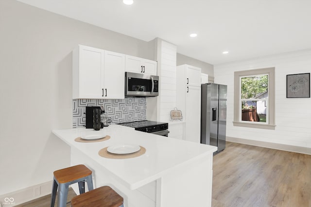 kitchen featuring stainless steel appliances, light hardwood / wood-style floors, white cabinetry, a kitchen bar, and kitchen peninsula