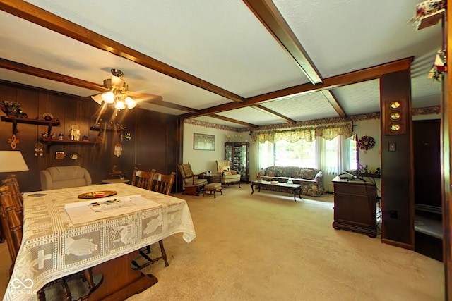 carpeted dining space with ceiling fan, wood walls, and beamed ceiling